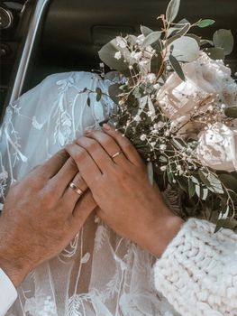 Elegant hands of newlyweds adorned with rings and holding a bouquet.