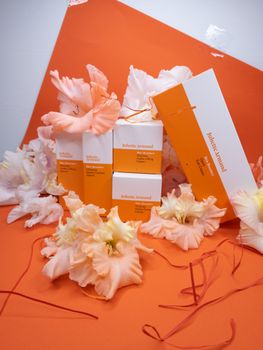 Colorful skincare products surrounded by delicate flowers on an orange background.