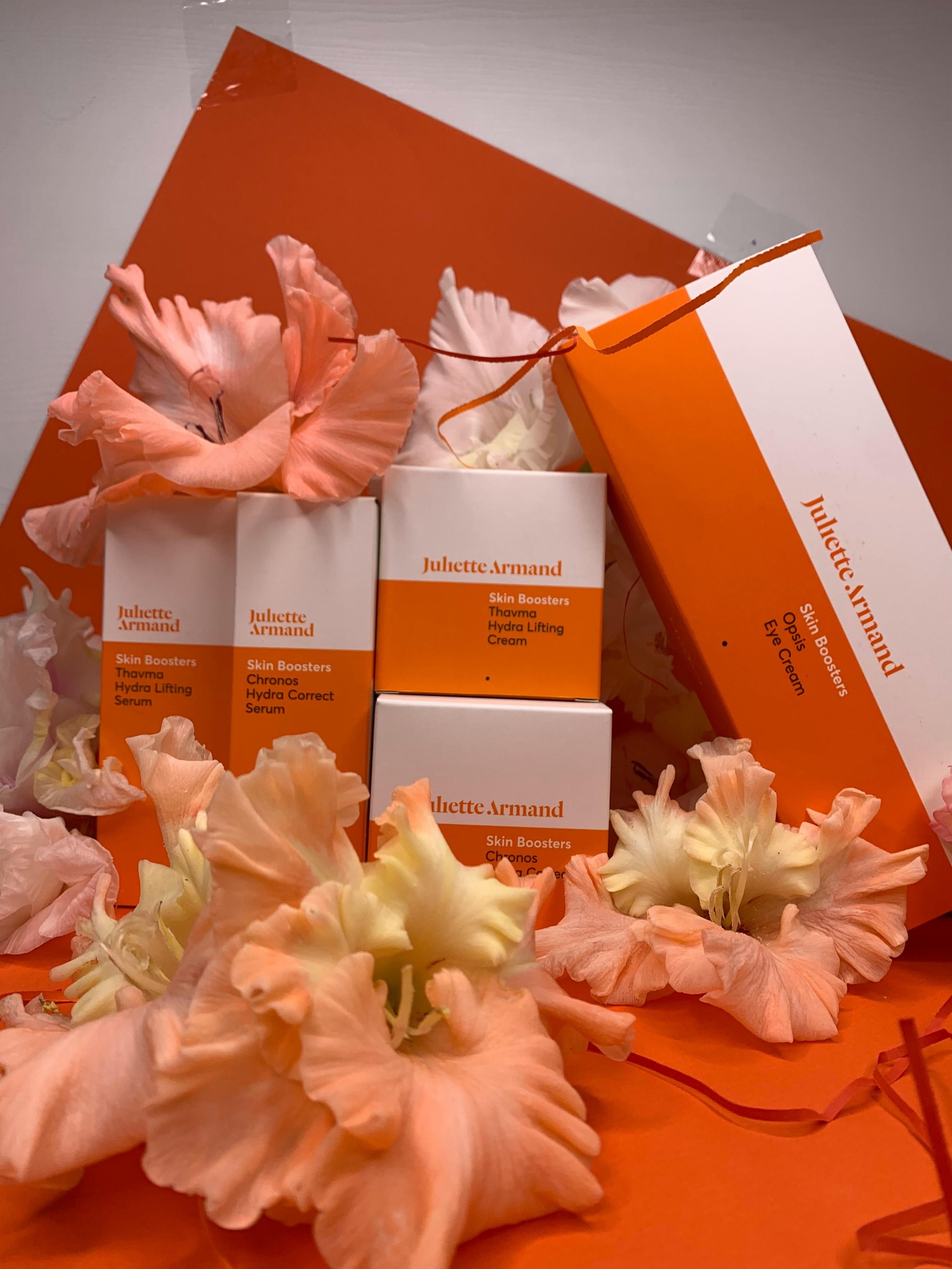 Vibrant skincare product setup with orange packaging and pastel flowers for a fresh aesthetic.