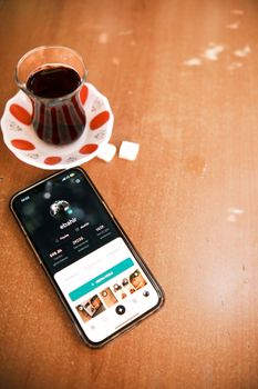 Close-up of smartphone with social media app next to Turkish tea and sugar cubes.