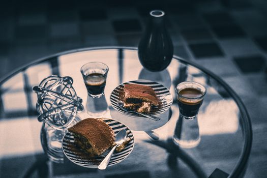 Tiramisu slices and espresso cups on a reflective glass table create a classic and elegant setting.
