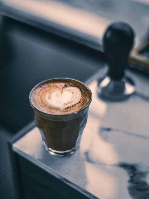 Free A stylish macchiato with heart-shaped latte art served on a marble table, with soft lighting enhancing the cozy ambiance. Stock Photo
