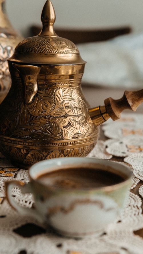 Free A traditional brass coffee pot and cup on a lace tablecloth, depicting a cozy, vintage coffee setting. Stock Photo
