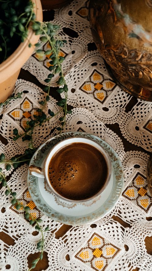Free Elegant vintage coffee setup with porcelain cup on lace tablecloth, surrounded by greenery. Stock Photo