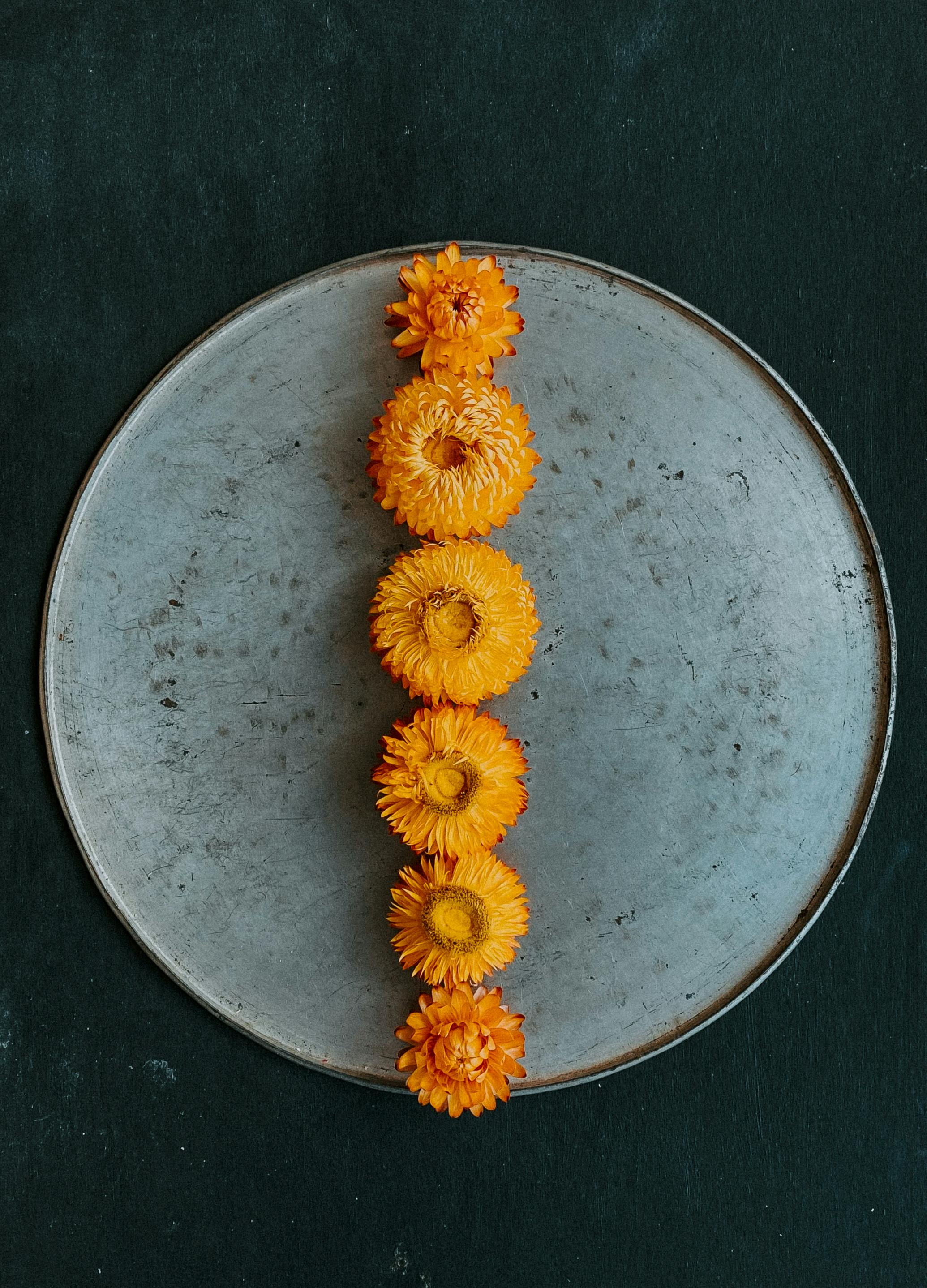 Aesthetic arrangement of bright orange flowers on a rustic round plate, perfect for autumn-themed design.