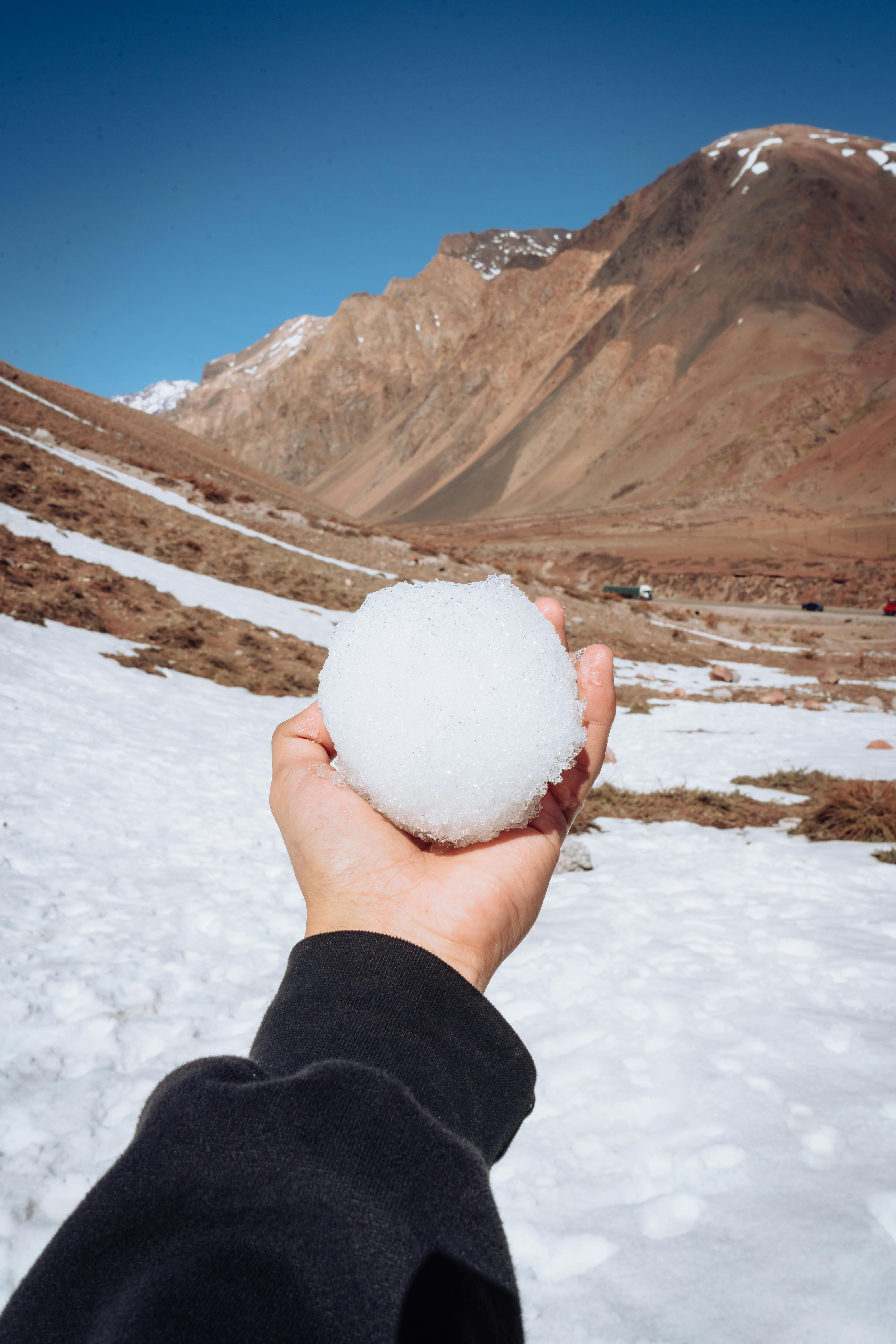 A hand holding a snowball against the backdrop of Los Penitentes mountains in Mendoza, Argentina.