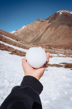 A hand holding a snowball against the backdrop of Los Penitentes mountains in Mendoza, Argentina.