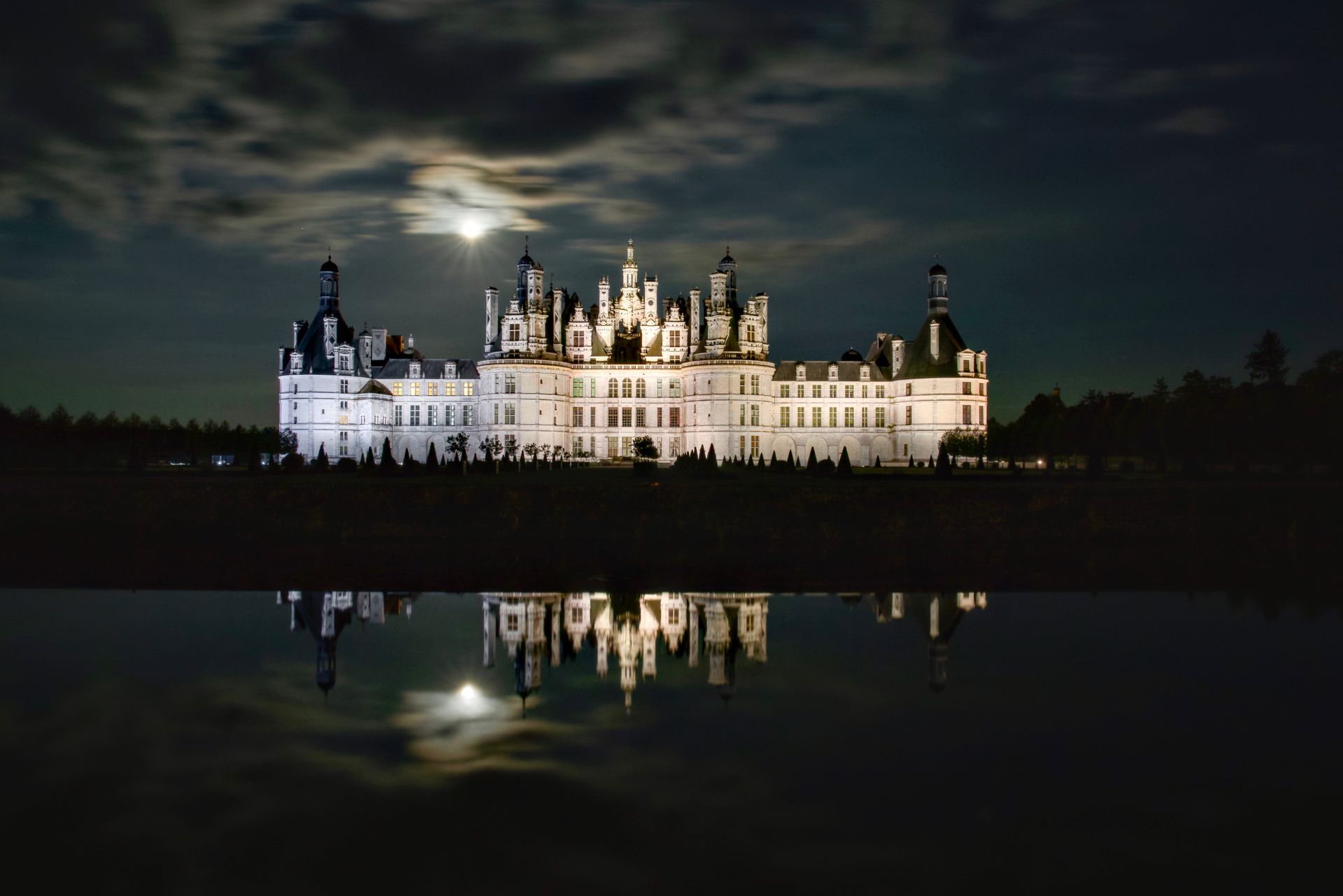 Majestic Château de Chambord illuminated under moonlight, reflecting in water.