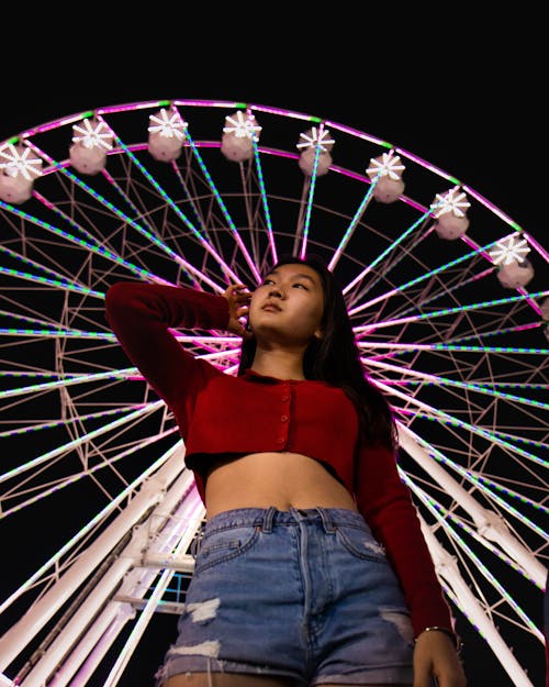 Free Low-Angle Shot of a Woman in a Red Crop Top Posing Near a Ferris Wheel Stock Photo