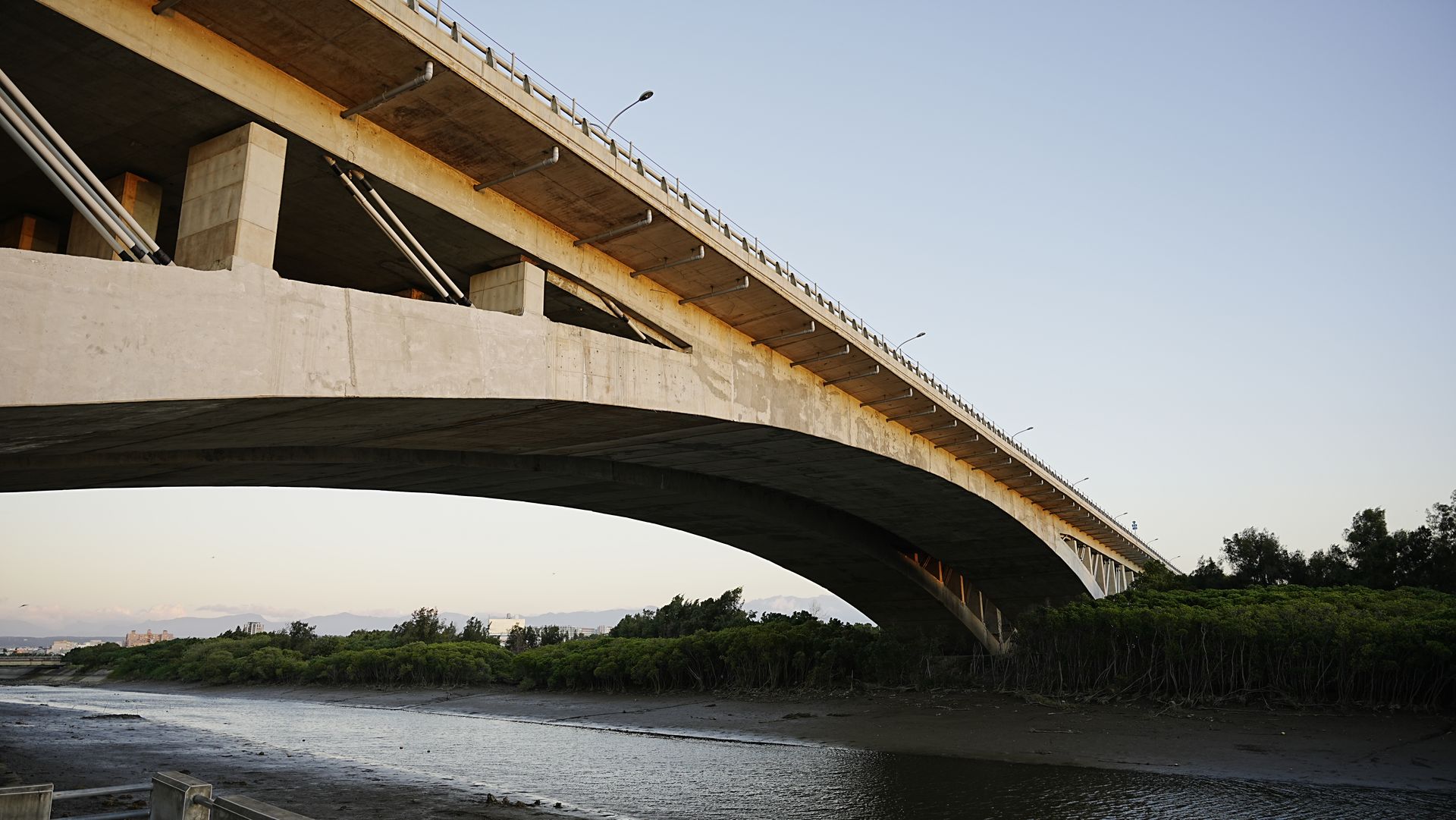 Concrete bridge spanning over a river with scenic view and clear sky.