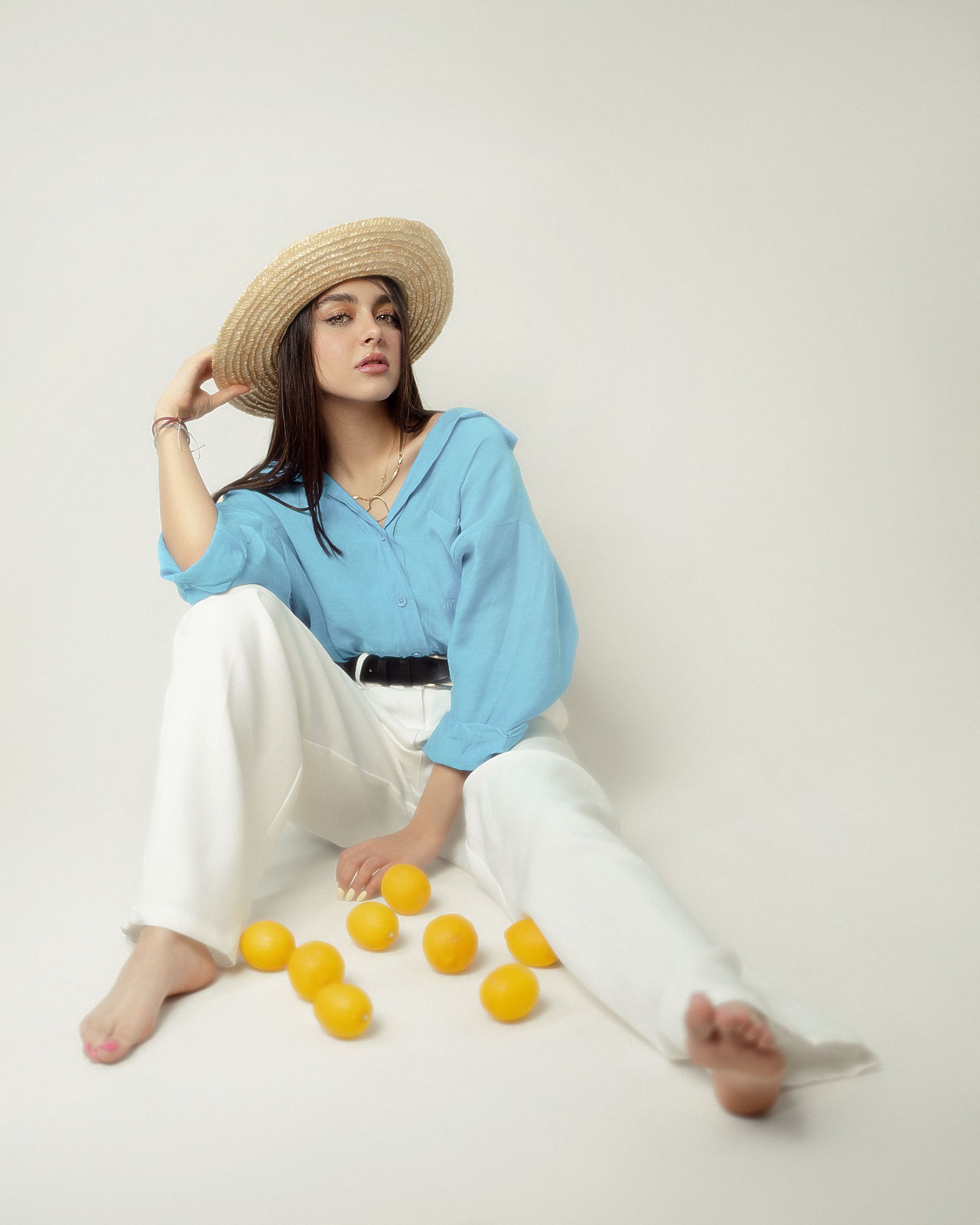 Chic woman in straw hat posing with lemons, wearing blue and white, modern fashion