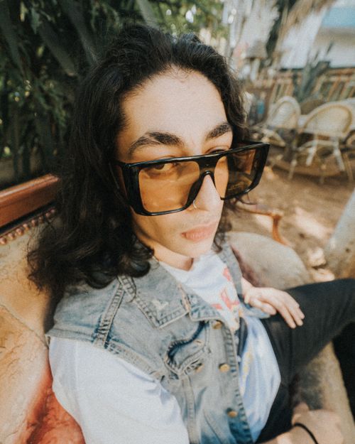 Free A person with long hair wearing sunglasses and denim jacket seated indoors with a relaxed demeanor. Stock Photo