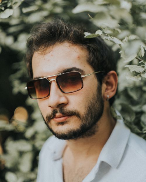 Free Portrait of a man with sunglasses surrounded by lush foliage, exuding calmness. Stock Photo