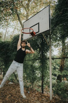 A young man skillfully dunking on a basketball court amid lush green foliage in Antalya, Türkiye.