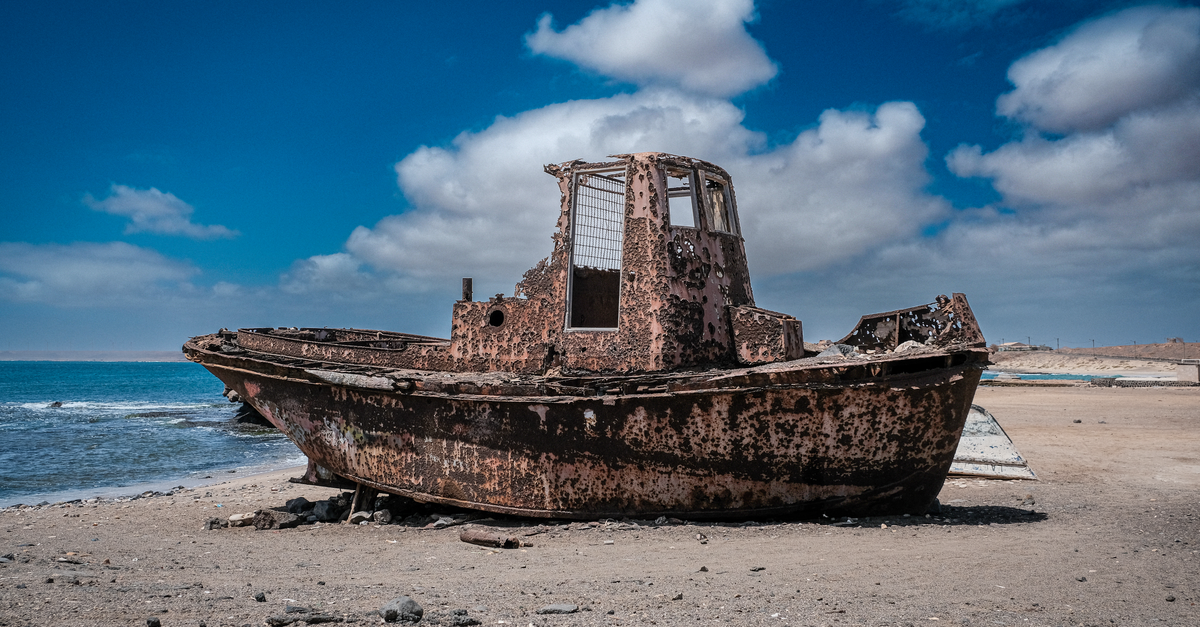 An abandoned rusty boat on the sandy shores of Pedra Lume, Sal Island, under a vivid blue sky.