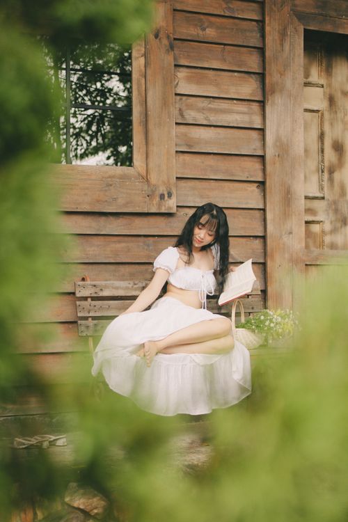Free Tranquil scene of a woman in white dress sitting by wooden wall in Vietnam. Stock Photo