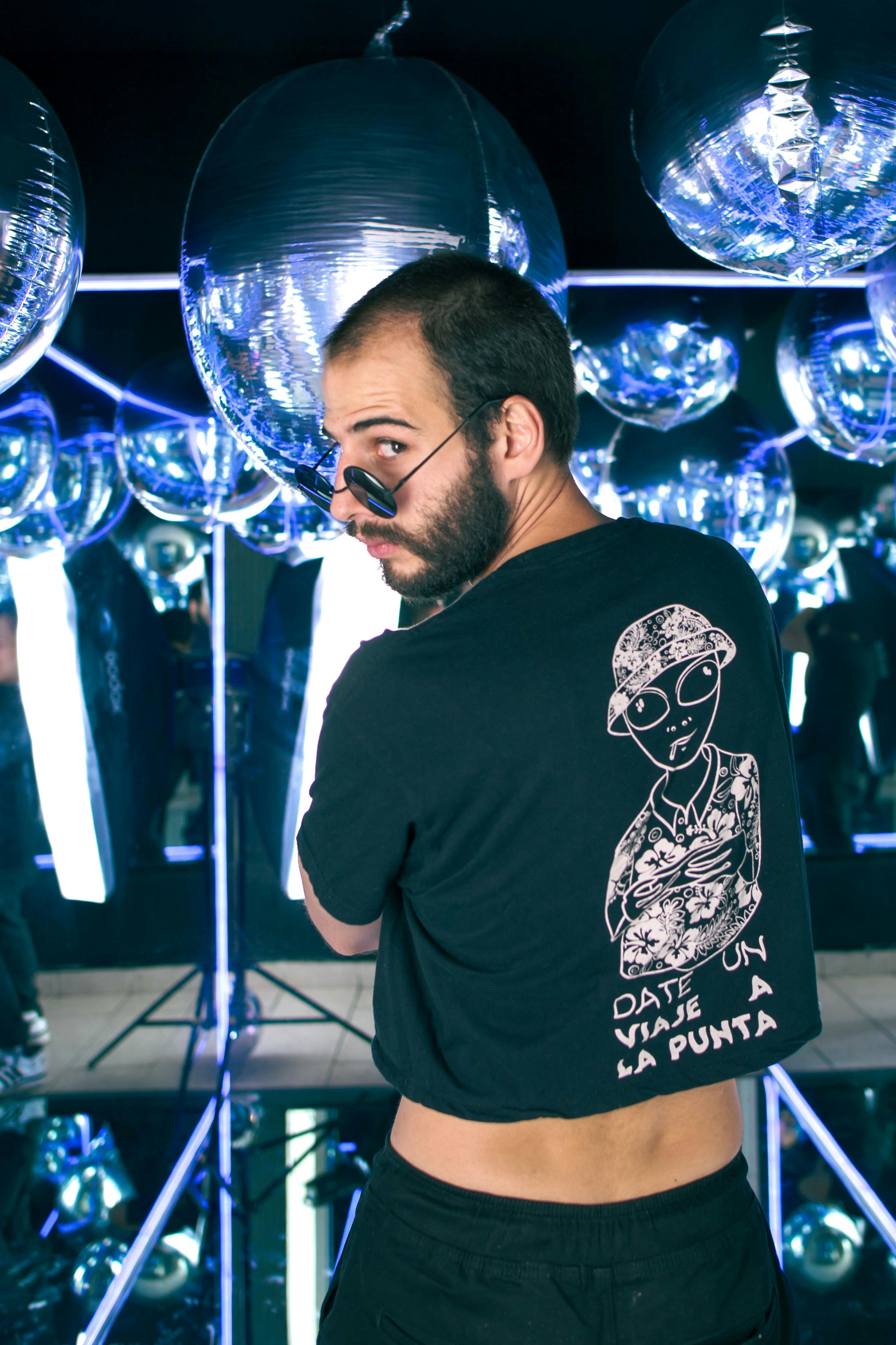 Man in a reflective disco room with spheres, wearing sunglasses and a graphic tee.