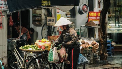 Free A vendor in Hanoi's street market with traditional hat, selling vegetables and fruits. Stock Photo