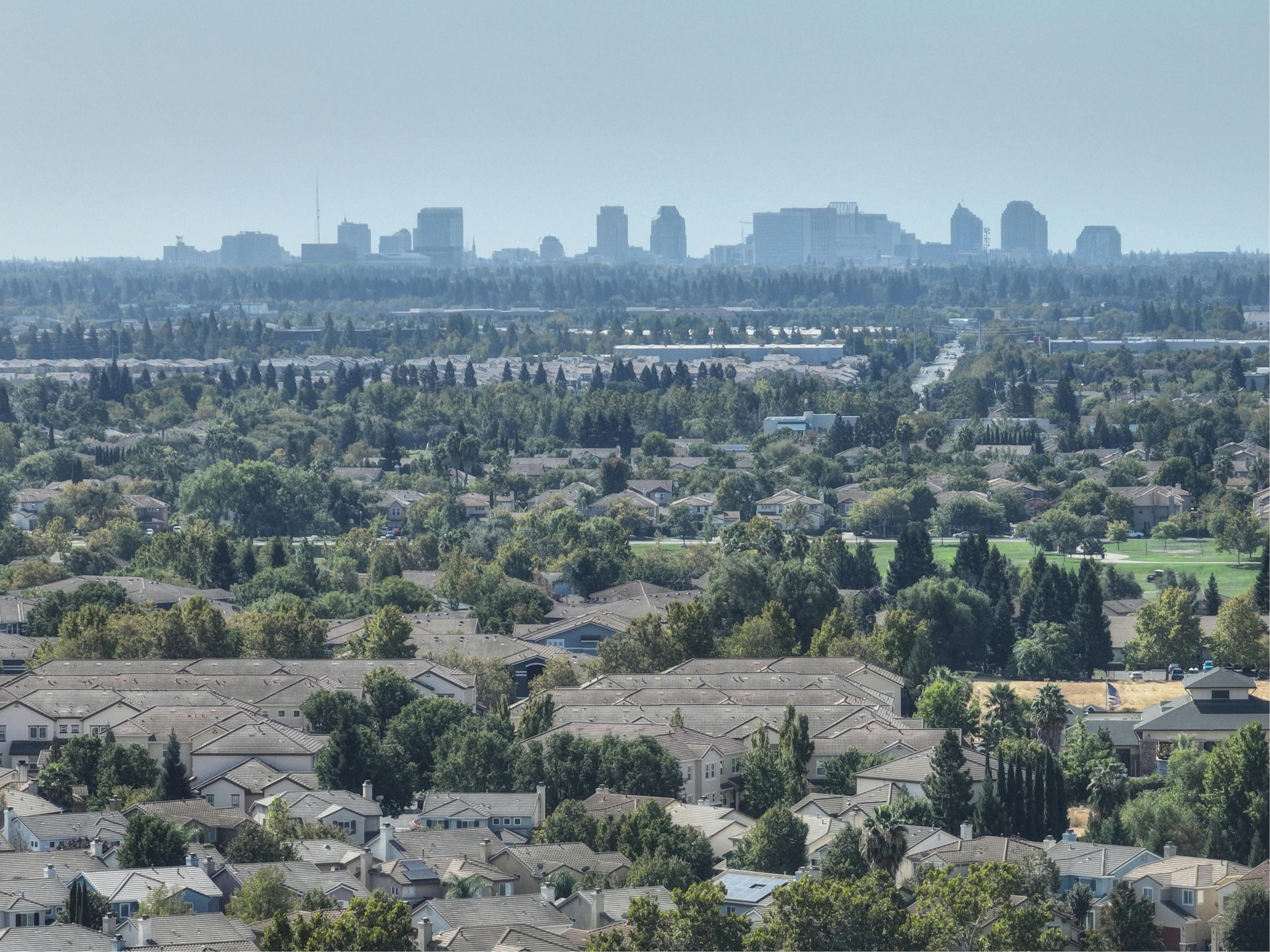Aerial view of Sacramento's suburban homes with the city skyline in the distance. Lush greenery and clear skies.
