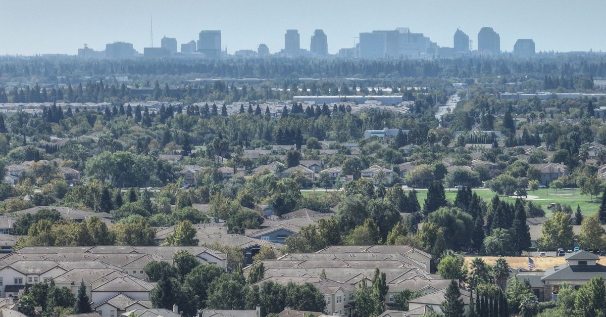 Aerial view of Sacramento's suburban homes with the city skyline in the distance. Lush greenery and clear skies.