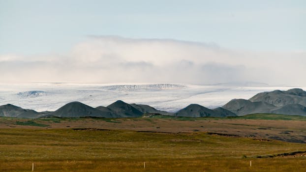 Peaceful countryside with green fields and distant snowy mountains under a clear sky.