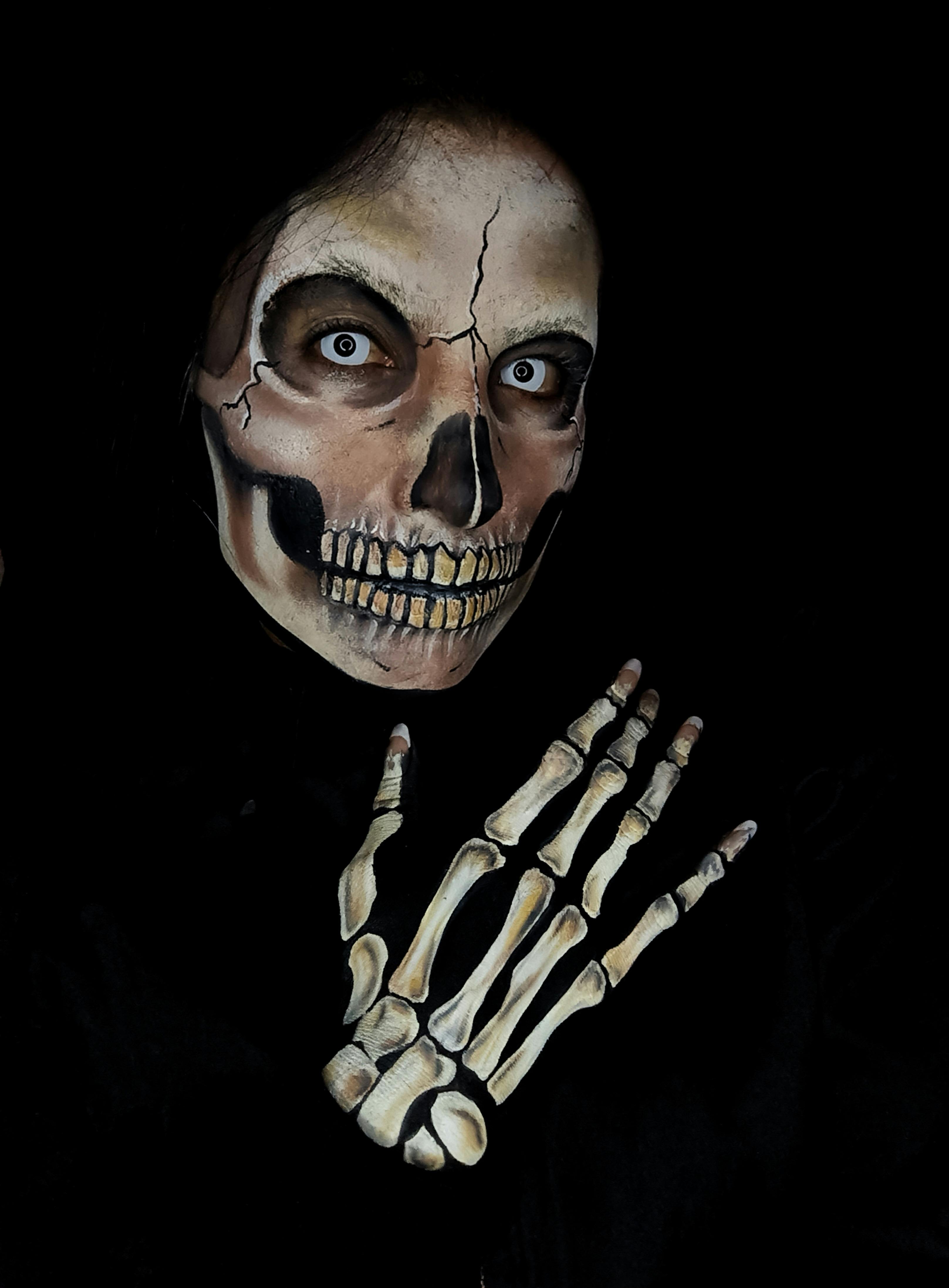 Close-up of eerie skull face paint with skeletal hand on dark background.