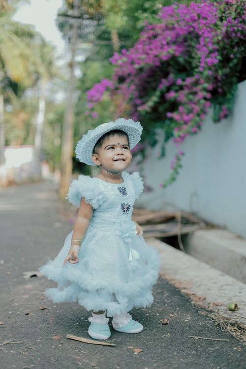 Free Charming baby girl in a blue dress and hat, with flowers, smiling outdoors. Stock Photo