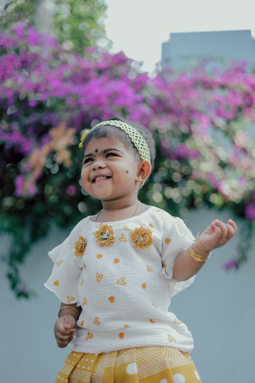 Free A cheerful baby in a sunny outfit smiling with a vibrant floral background. Stock Photo