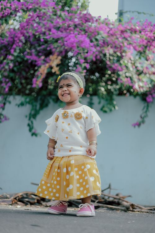 Free Adorable baby smiling in yellow polka dot skirt in front of vibrant flowers. Perfect for lifestyle content. Stock Photo