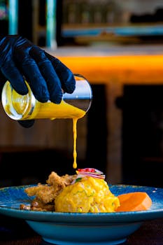 A vibrant dish with sauce poured by a gloved hand, highlighting culinary artistry.