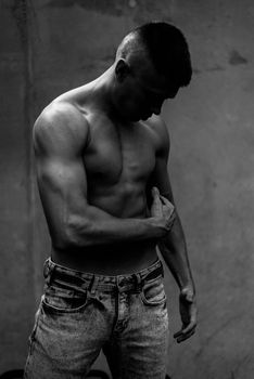 Black and white portrait of a muscular man in casual jeans posing against a textured wall.