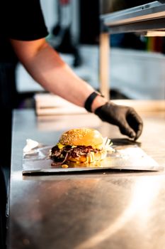 A chef places a delicious gourmet burger on a tray, highlighting fresh ingredients.