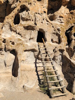 Wooden ladder against a rocky cliff leading to a cave entrance in bright sunlight.