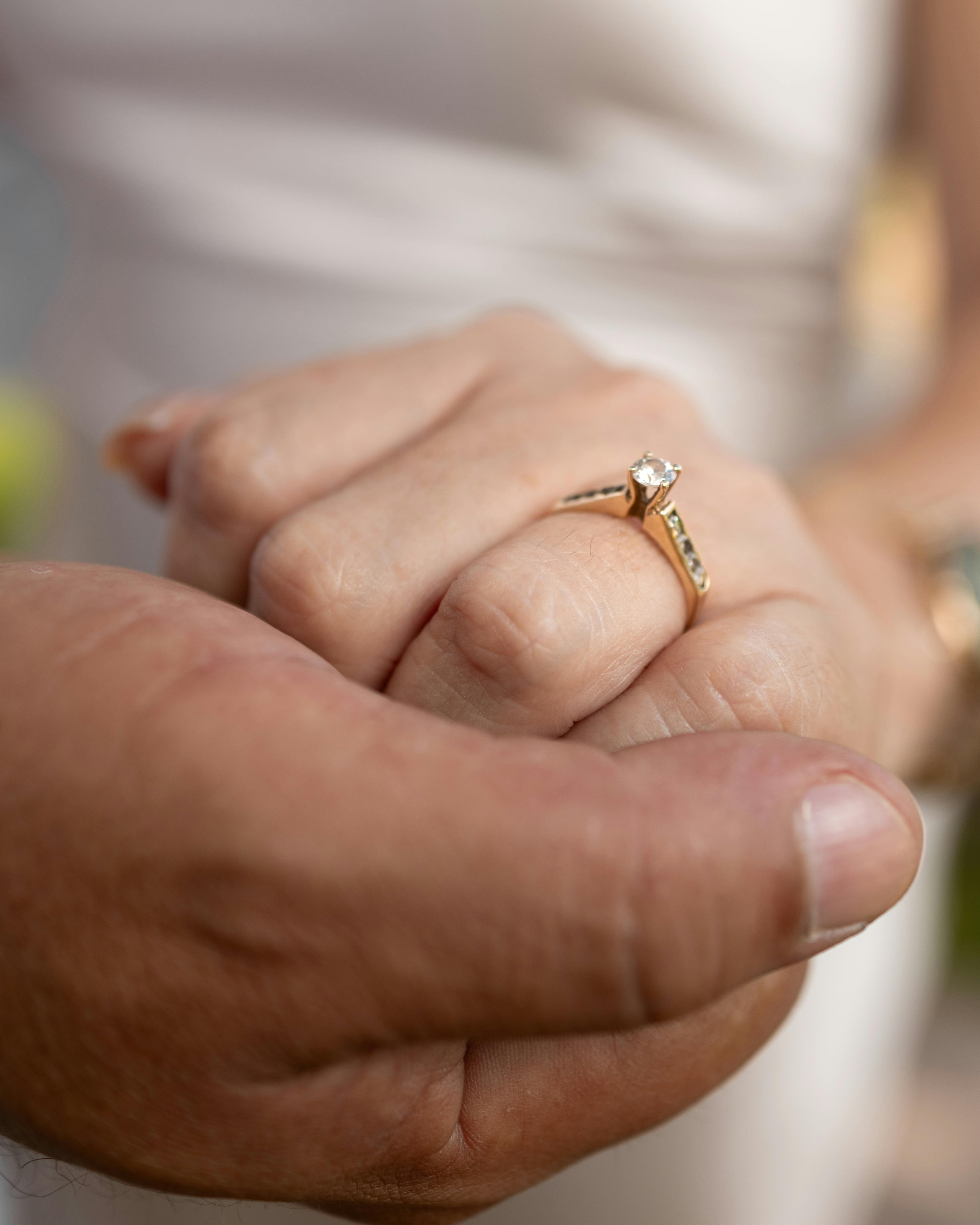 A couple holding hands, showcasing an elegant engagement ring in an outdoor setting.