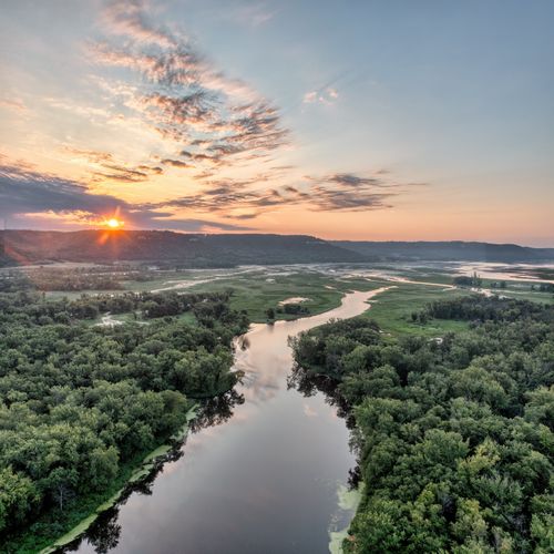 Free A serene sunrise over the Mississippi River with lush greenery in Wabasha, MN, USA. Stock Photo