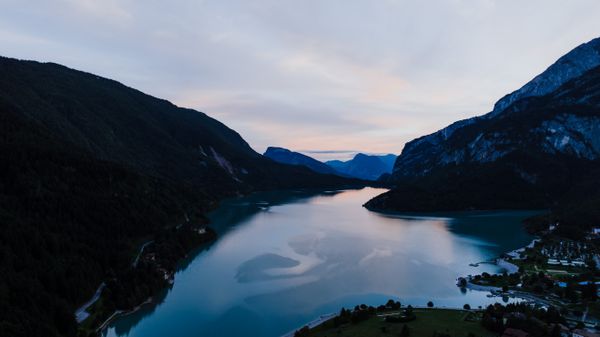 Still alpine lake between steep forested slopes — photo by K on Pexels