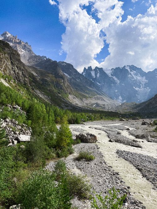 Free Breathtaking view of alpine mountains, lush greenery, and flowing river under a blue sky. Stock Photo