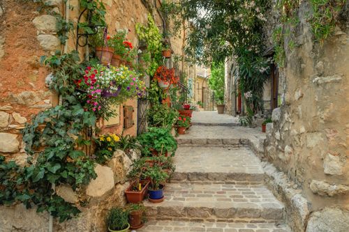 Free Beautiful cobblestone alley in France adorned with colorful flowers and stone architecture. Stock Photo