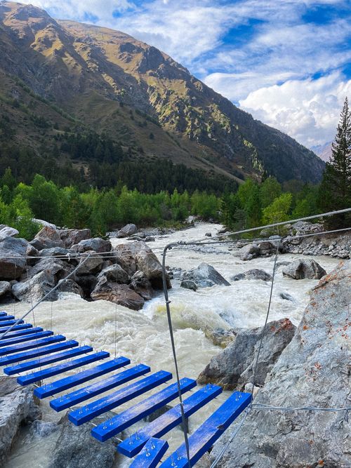 Free Breathtaking view of a mountain river with a rustic blue bridge and lush greenery. Stock Photo
