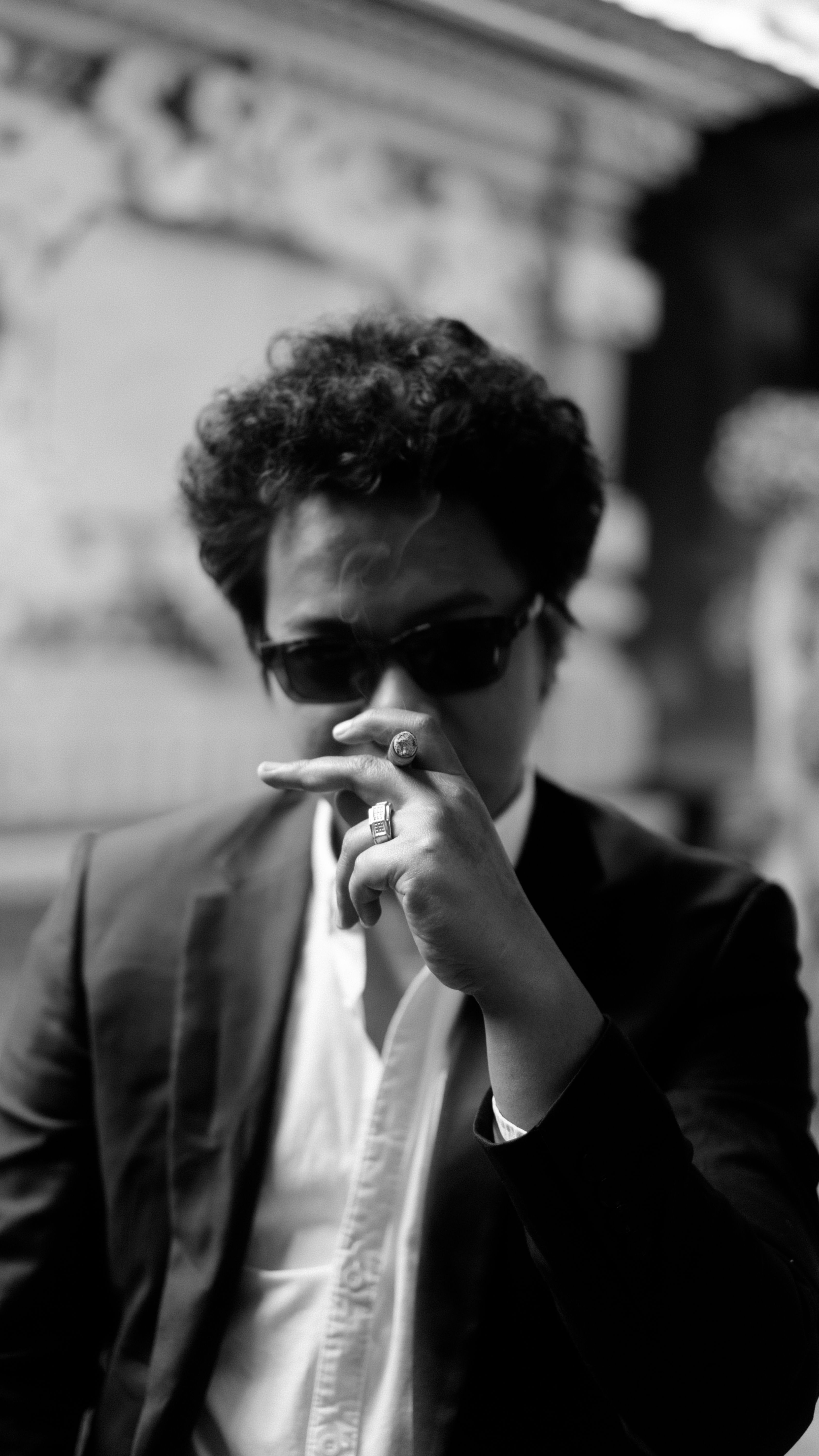 A man in a black suit and sunglasses poses confidently, creating a mysterious and stylish vibe.