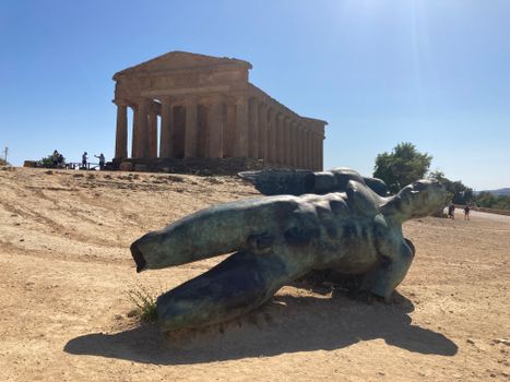 Temple of Concordia in Agrigento, Sicily with a modern sculpture in the foreground under a bright summer sky.