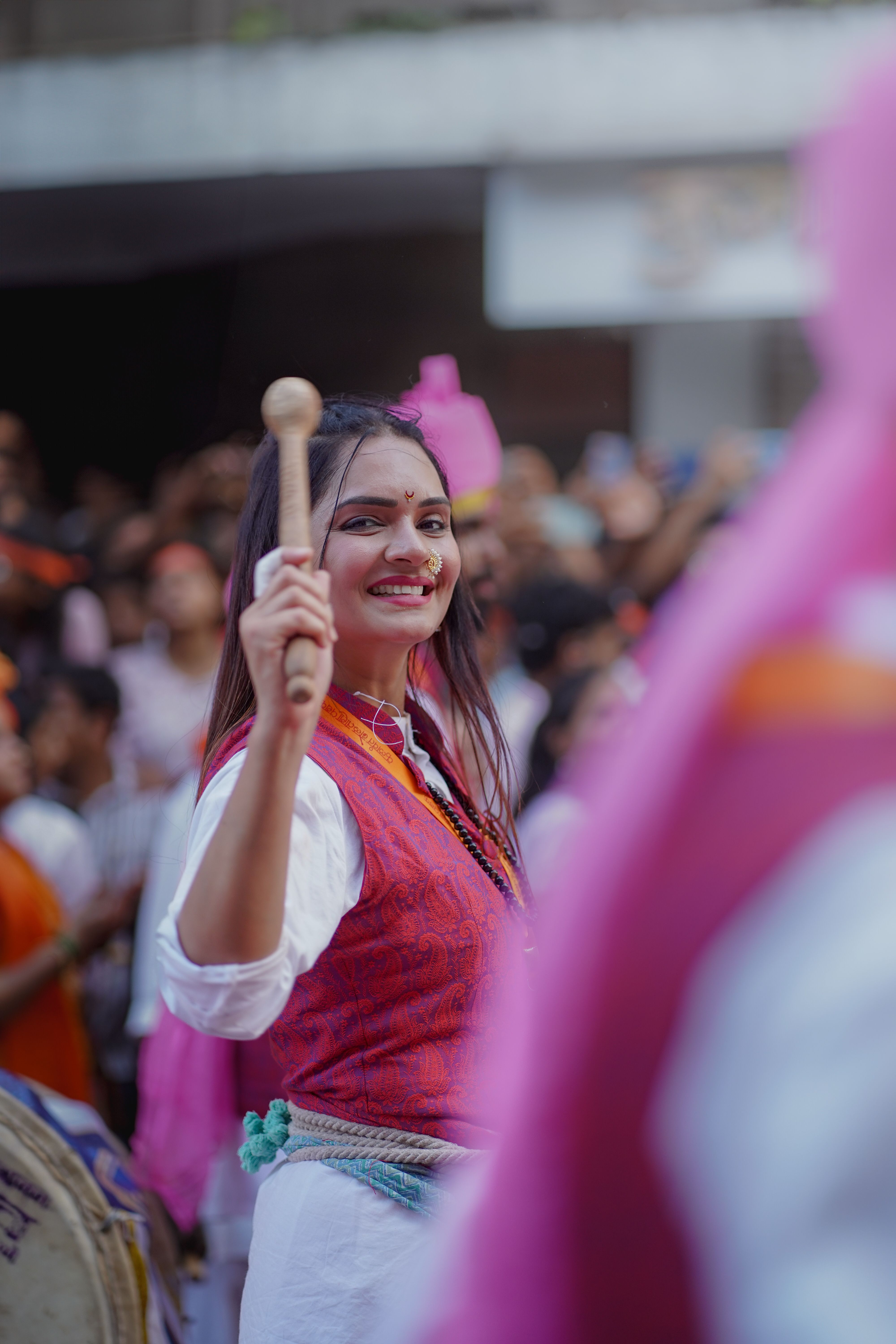 Young woman joyfully participates in Ganesh Chaturthi festival, Pune, with colorful attire and happy expressions.