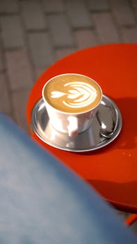 Latte art in a white cup on a red table outdoors, perfect for cozy moments.