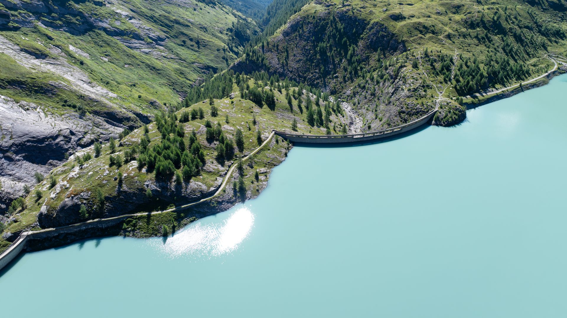 A stunning aerial view of the dam and turquoise lake in Korutany, with lush green landscapes and clear blue skies.