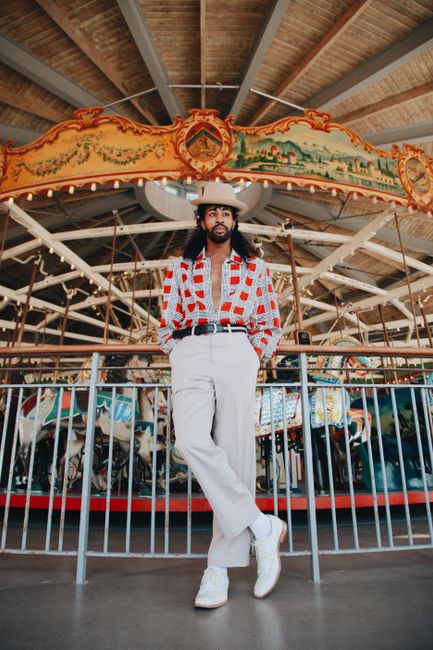 Stylish man posing in front of a decorative vintage carousel indoors.