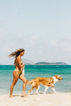 A woman walks with her dog on a sunny beach in Rio de Janeiro, Brazil.