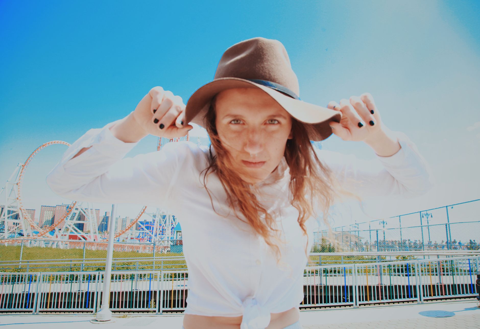 Stylish woman with sun hat poses outdoors with ferris wheel background.