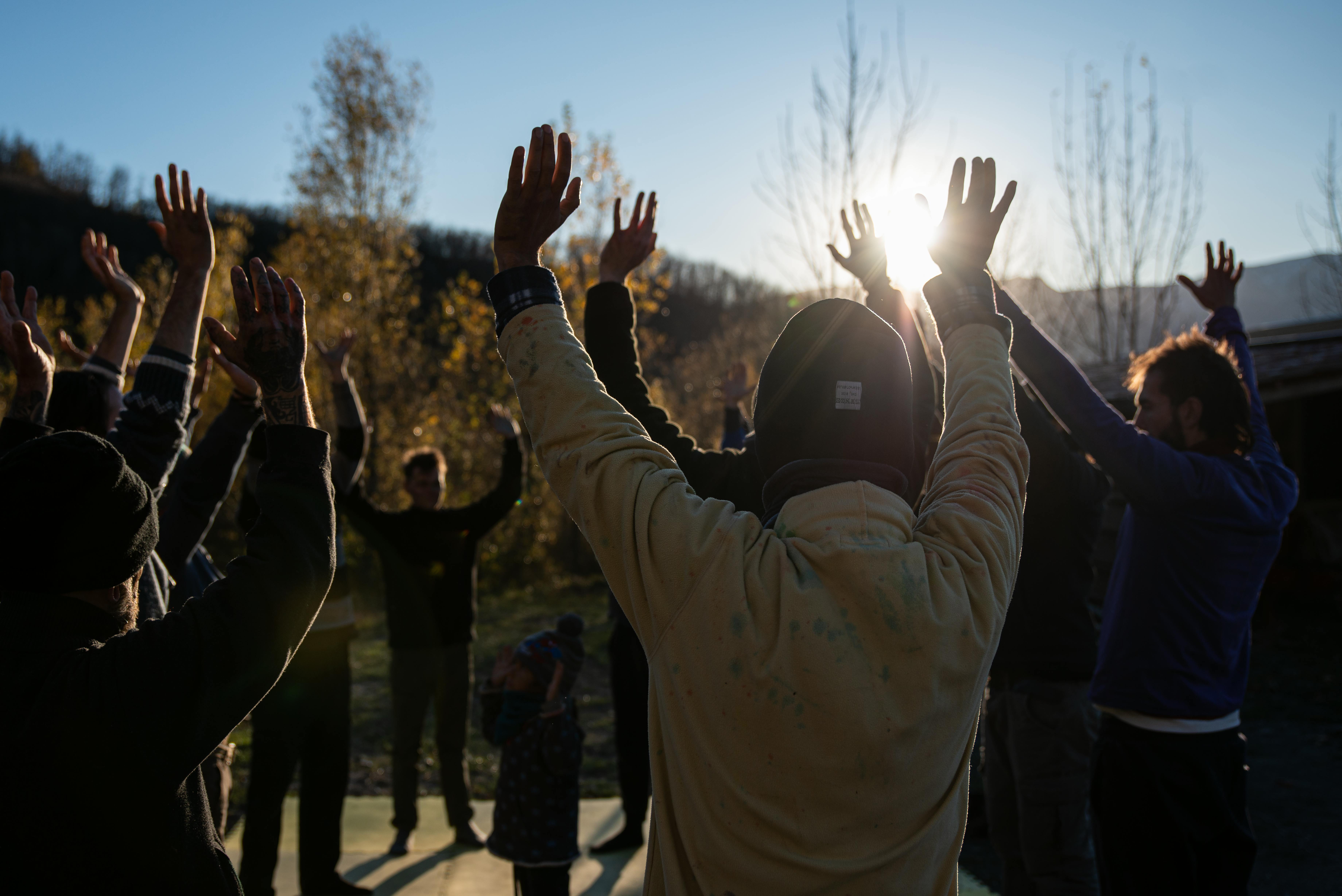 Group of people raising arms outdoors during sunrise for a refreshing exercise session.