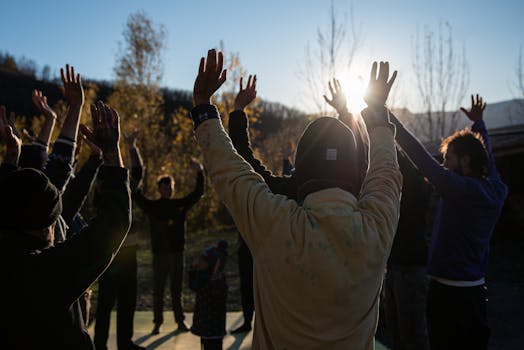 Group of people raising arms outdoors during sunrise for a refreshing exercise session.