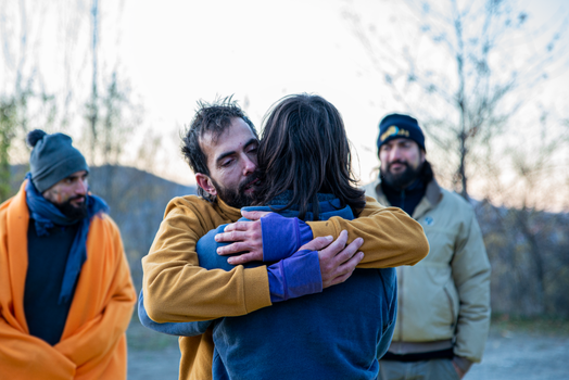 A heartfelt hug between friends outdoors during a cool, bright day.